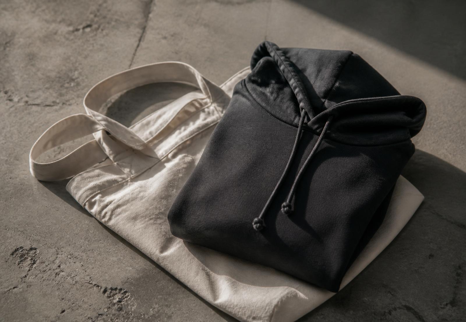 A folded hoodie and long sleeve on a concrete floor