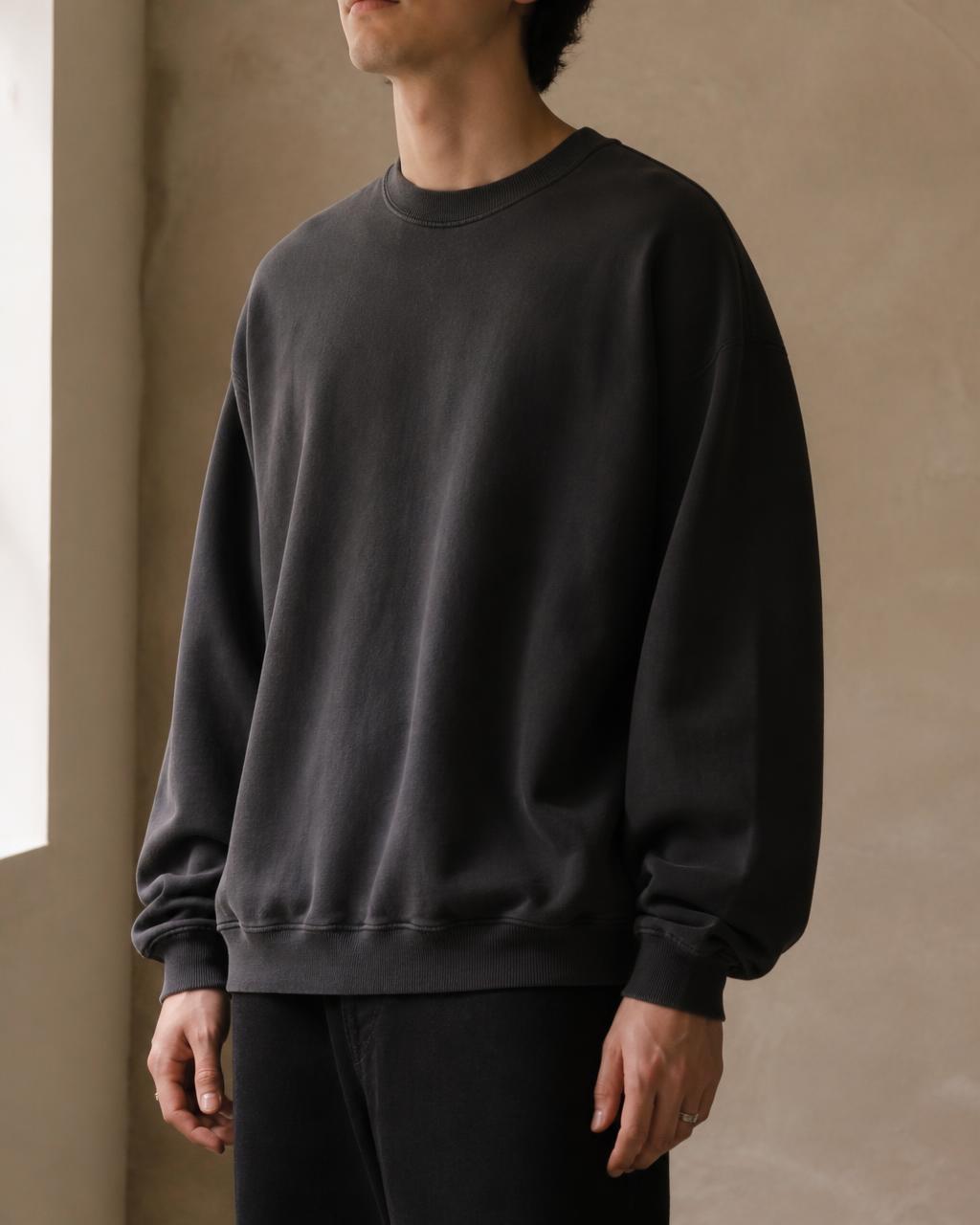 Model wearing a charcoal crew sweatshirt — “still here. still counts.”
